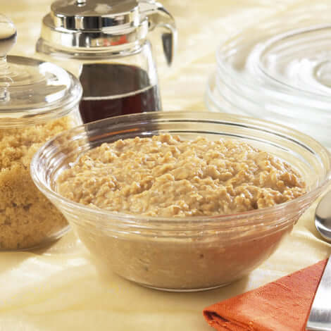 Creamy protein oatmeal in a clear bowl, with brown sugar and syrup in the background, perfect for a nutritious breakfast.
